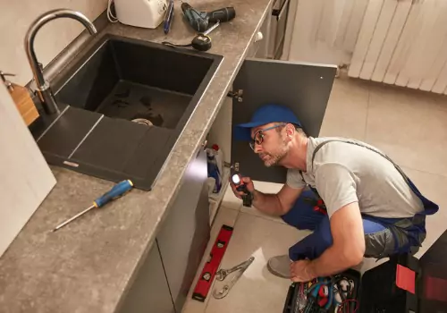 A plumber is seen working on a kitchen sink. TCI Plumbing performs Plumbing in Peoria IL.