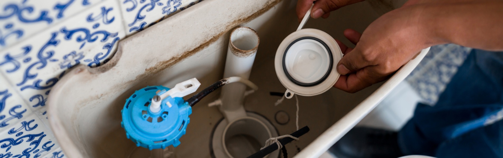 A close-up on a plumber from TCI Plumbing, which offers residential plumbing services, fixing a toilet in the bathroom.
