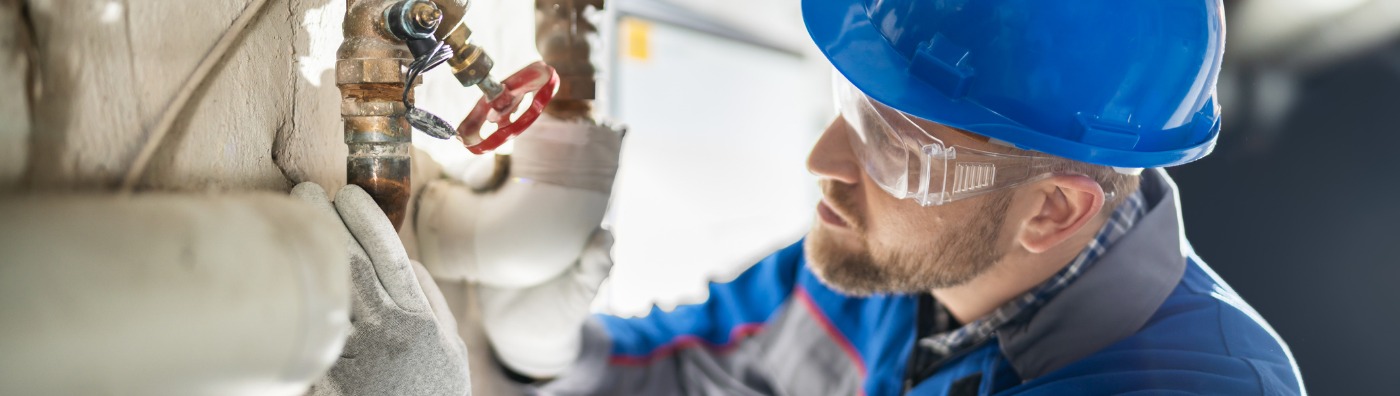 A male plumber inspecting a building's pipe, performing essential commercial plumbing service