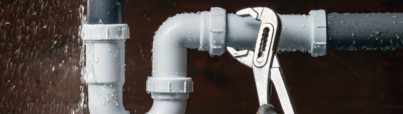 A plumber fixing a leaky pipe under a sink, part of the plumbing & utility services offered by TCI Companies