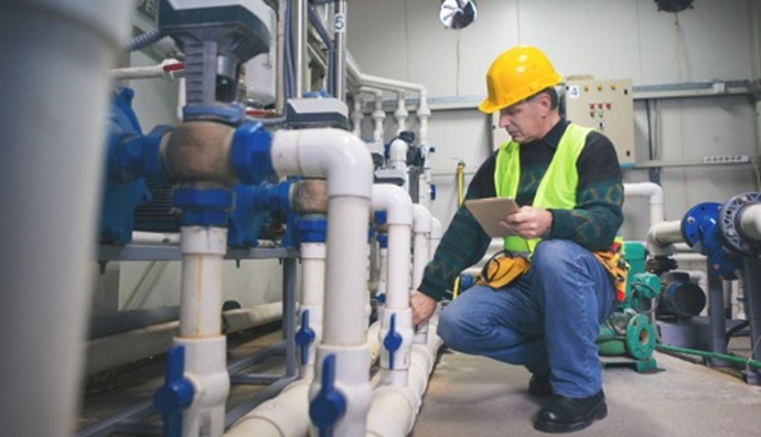 A professional plumber checking a boiler room's pipes to track down the source of a leak, as a part of TCI Companies' commercial plumbing services
