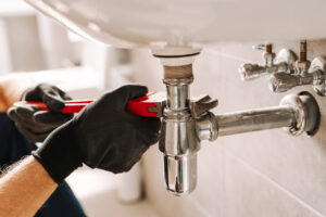 A Peoria Plumber fixes a sink pipe with a wrench in a bathroom, showcasing precision and craftsmanship